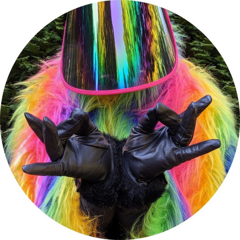 Hände in schwarzen Lederhandschuhen machen eine Geste vor einer verspiegelten Maske mit Fellkragen in Regenbogenfarben