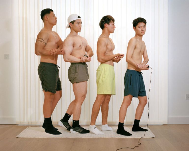 Vier asiatische junge M&auml;nner in Boxershorts stehen hintereinander in Pose, um ihre Muskeln zu zeigen
